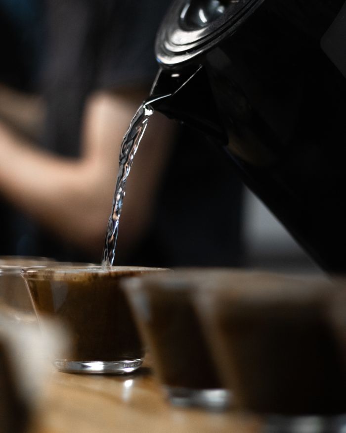 Água caindo da chaleira sobre o café moído em um copo de prova.